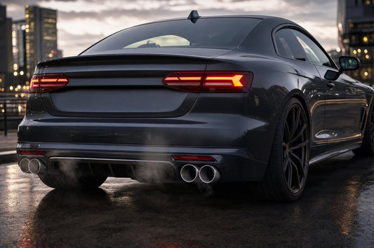 Low rear view of a dark grey performance coupe at dusk with quad stainless steel exhaust tips under a black rear diffuser