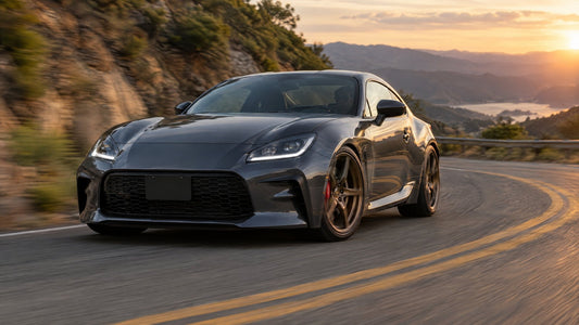 Dark gray second-generation Toyota GR86 sports coupe with bronze forged wheels and red big brake calipers cornering on a mountain road at sunset