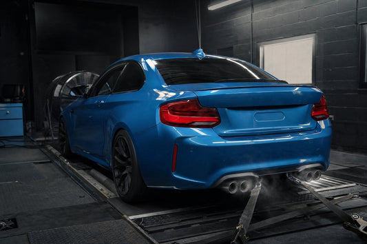 Blue BMW F87 M2 strapped to a chassis dyno, rear three-quarter view with quad exhaust tips