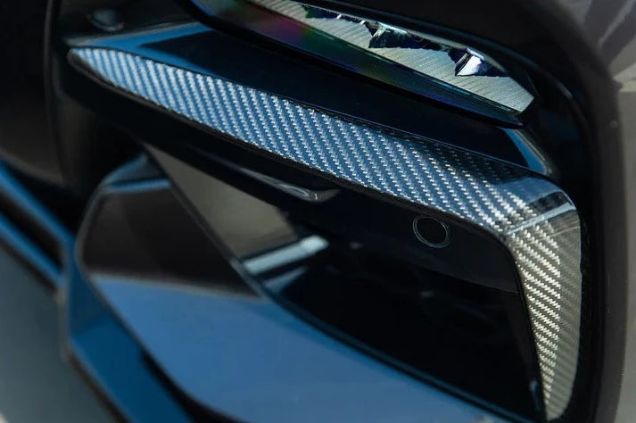 A front close up view of AUTOTECKNIC CARBON FIBER FRONT BUMPER TRIM SET - BMW G01 X3 | G02 X4 M40I PRE-LCI 2017-2021 fitted on a dark blue car