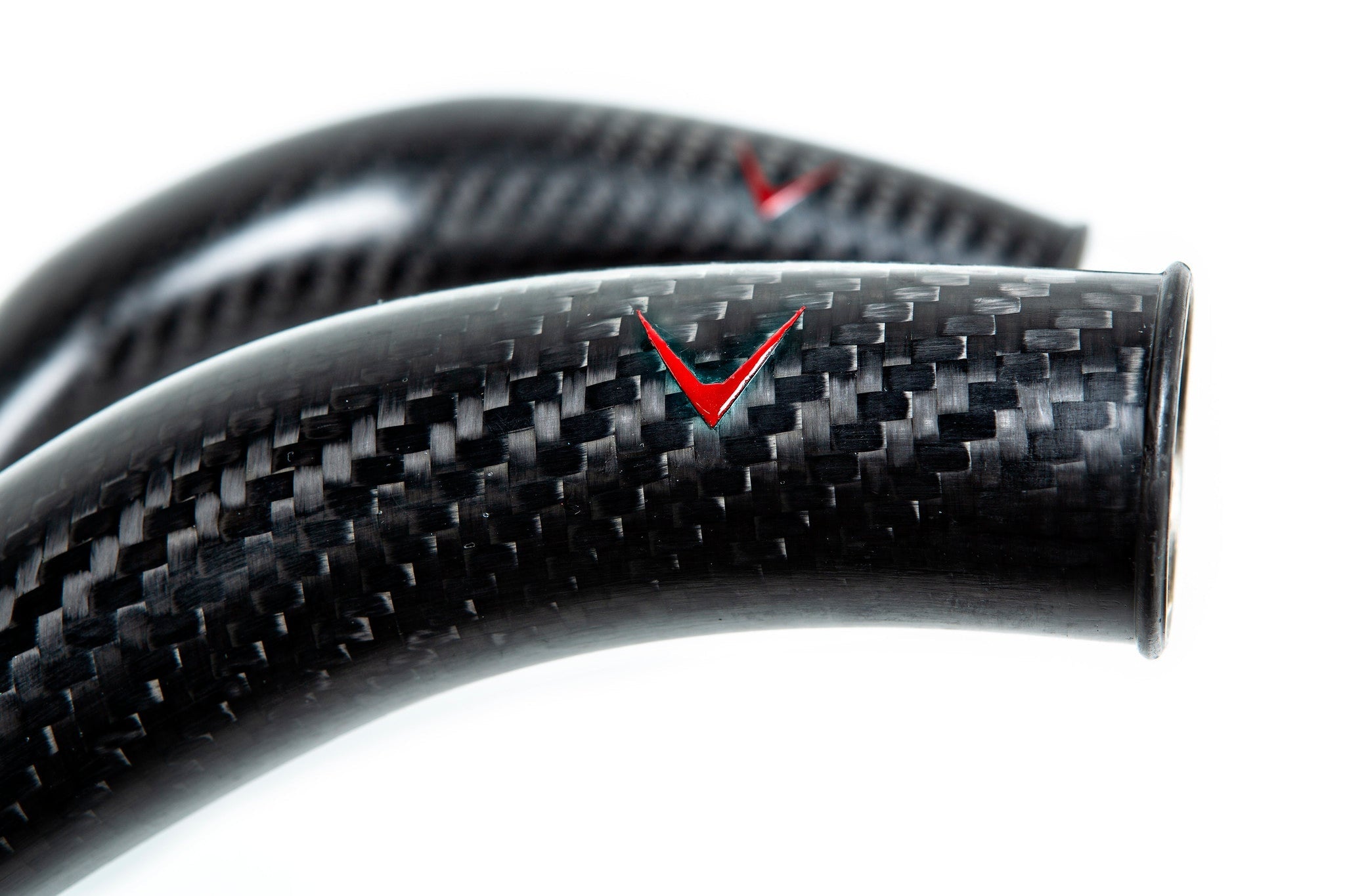 Close-up view of curved carbon fiber charge pipes with glossy finish showing detailed weave pattern and red V logos - Eventuri charge pipes for BMW M3
