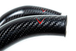 Close-up view of curved carbon fiber charge pipes with glossy finish showing detailed weave pattern and red V logos - Eventuri charge pipes for BMW M3