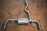A stainless steel valved axle-back exhaust system with brushed silver tips laid out on a brown concrete workshop floor.
