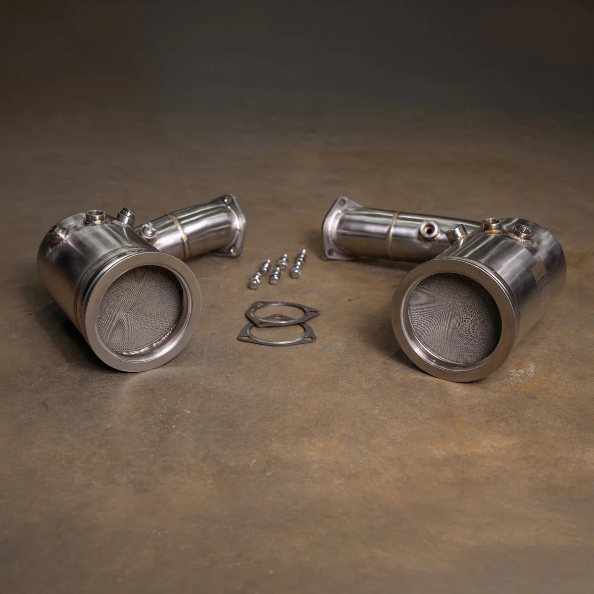 A pair of Valvetronic Designs 400 Cell Catted Downpipes for a 2019-2022 Lamborghini Urus, displayed on a concrete floor with accompanying mounting hardware and gaskets.