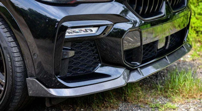 A close up view of a black car's front side fitted with AUTOTECKNIC PERFORMANCE DRY CARBON FRONT LIP SET - BMW G06 X6 M-SPORT 2023+