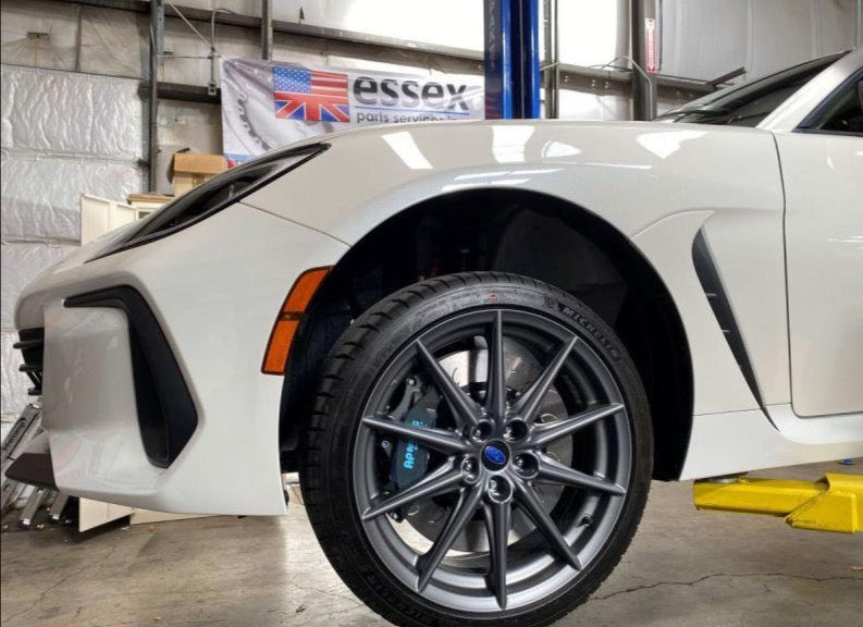 A close up view of a white car and its front wheel from the side fitted with AP Racing by Essex Radi-CAL Competition Brake Kit (Front CP9660/372mm) - Subaru BRZ, Scion FR-S & Toyota GT86/GR86 2013+