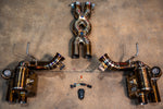 A top-down view of a gold-finish valved exhaust muffler with dual tips and a remote control module on a concrete floor.
