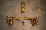 A full overhead view of the Valvetronic Designs gold-plated exhaust system components, including the X-pipe, dual valved mufflers, and remote control hardware laid out on a concrete floor.