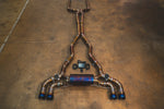 A full overhead view of the titanium valved exhaust system laid out on a concrete floor, showing the piping from the front flanges to the rear mufflers.