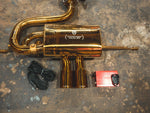 Close-up of a gold-finished Valvetronic Designs Special Ops exhaust muffler with dual tips, a red control box, remote, and wiring harness.