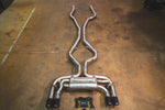 Overhead view of the full BMW X5M/X6M exhaust system including mid-pipes, valved muffler, quad carbon fiber tips, and wireless control module.