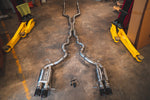 Overhead view of the full Valvetronic Designs stainless steel exhaust system laid out on a shop floor between two car lift arms.