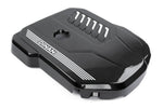 A high-gloss carbon fiber Dinan engine cover for BMW engines, featuring a vibrant 2x2 twill weave, white "Dinan" branding with accent stripes, and integrated cooling vents on a white background