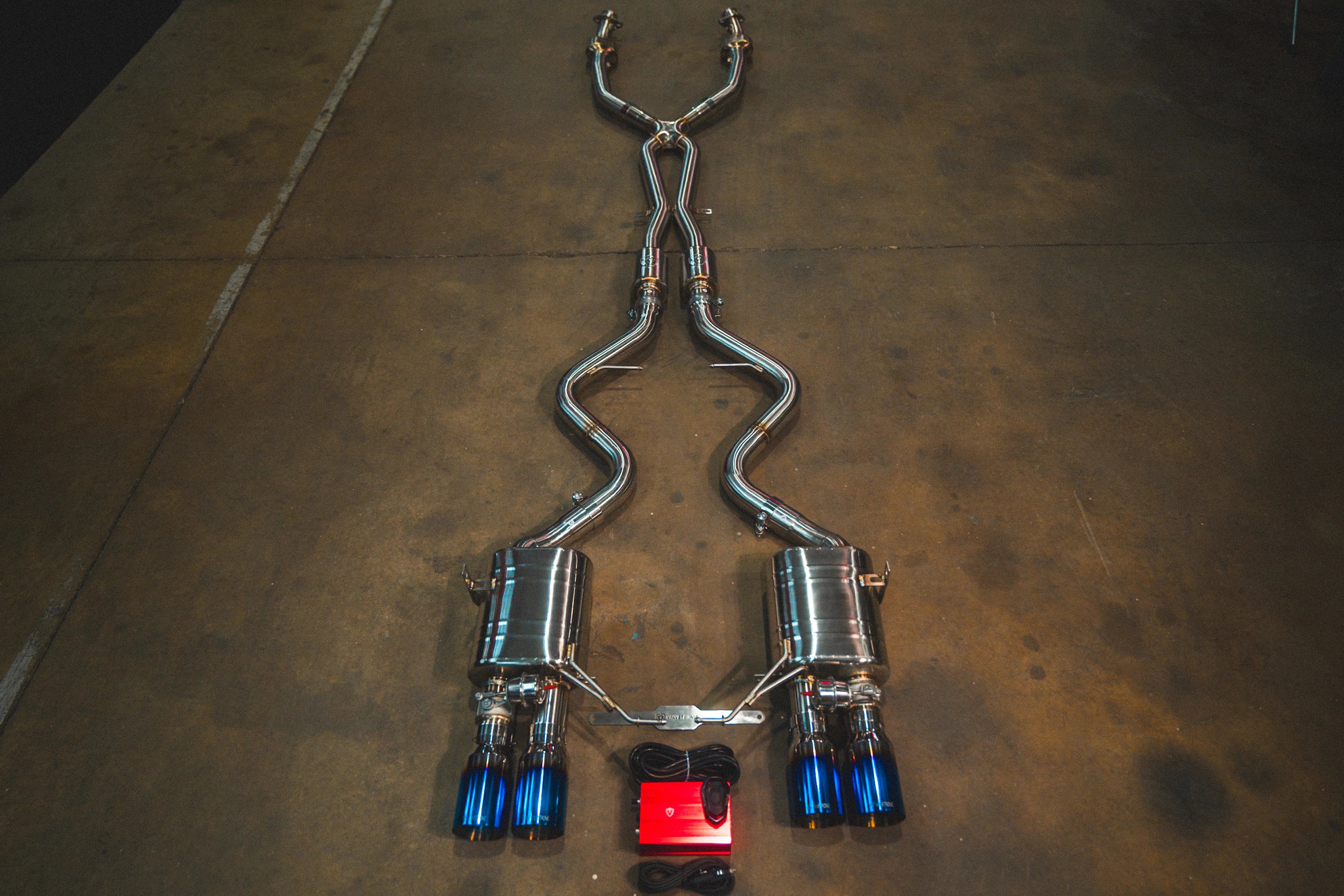 Full view of the Valvetronic Designs Valved Sport Exhaust System for BMW E9x M3 featuring quad burnt blue titanium exhaust tips and a red valve control module.