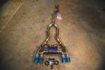 A full view of a titanium valved exhaust system for a BMW G87 M2 featuring quad exhaust tips with a blue and gold "burnt" titanium finish.