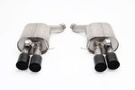 A studio product photo of the Dinan Free Flow Axle-Back Exhaust System for the 2012–2016 BMW M5, displayed on a solid white background. The system consists of two large, T304 stainless steel mufflers featuring a "straight through" canister design and high-quality TIG welds. Each muffler leads to dual 3.5-inch quad exhaust tips with a sleek black ceramic-coated finish and laser-engraved Dinan logos. The assembly includes mandrel-bent piping and factory-style mounting brackets for a direct bolt-on fitment.