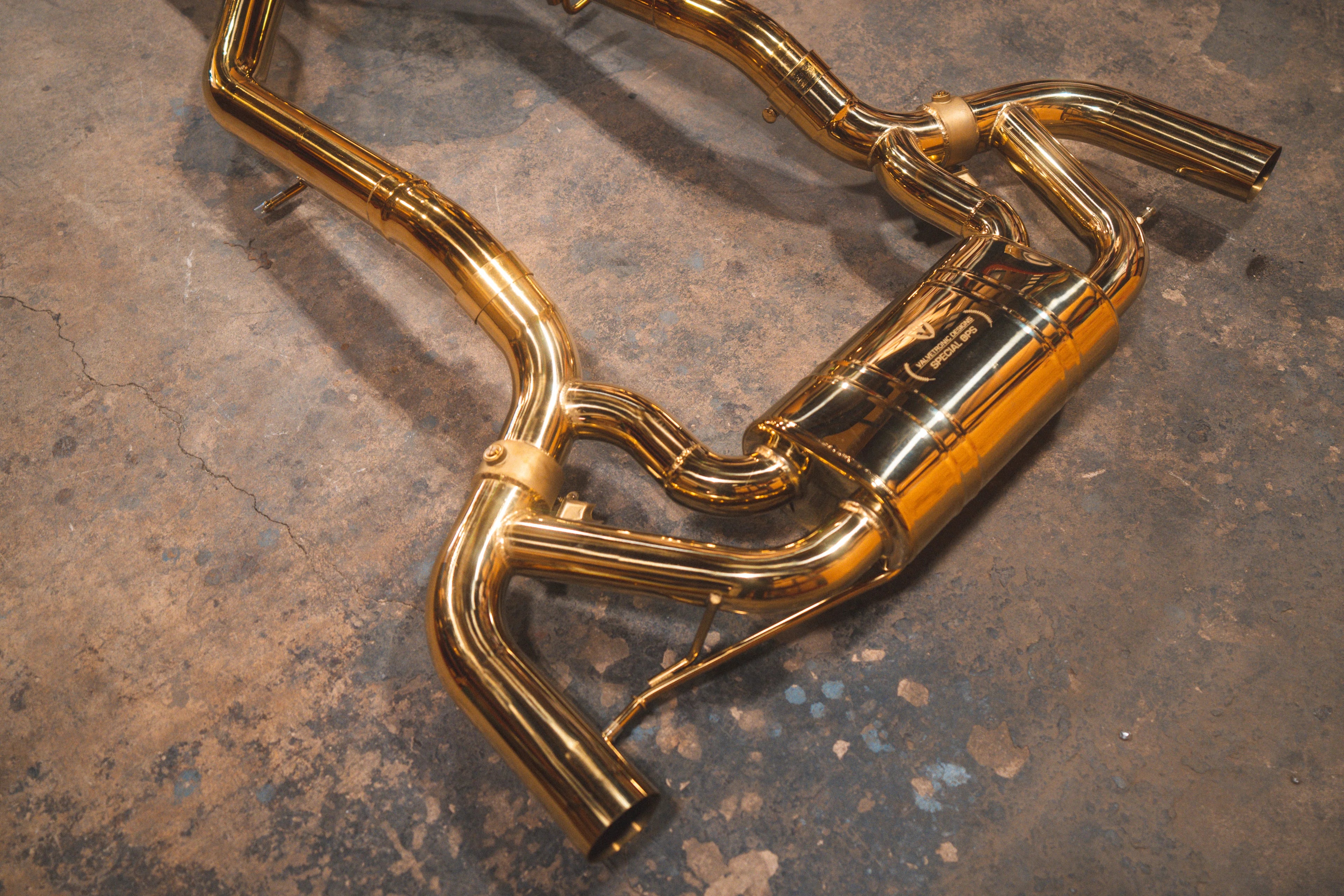 Close-up angled view of the rear muffler section and dual piping of the gold-plated exhaust system.