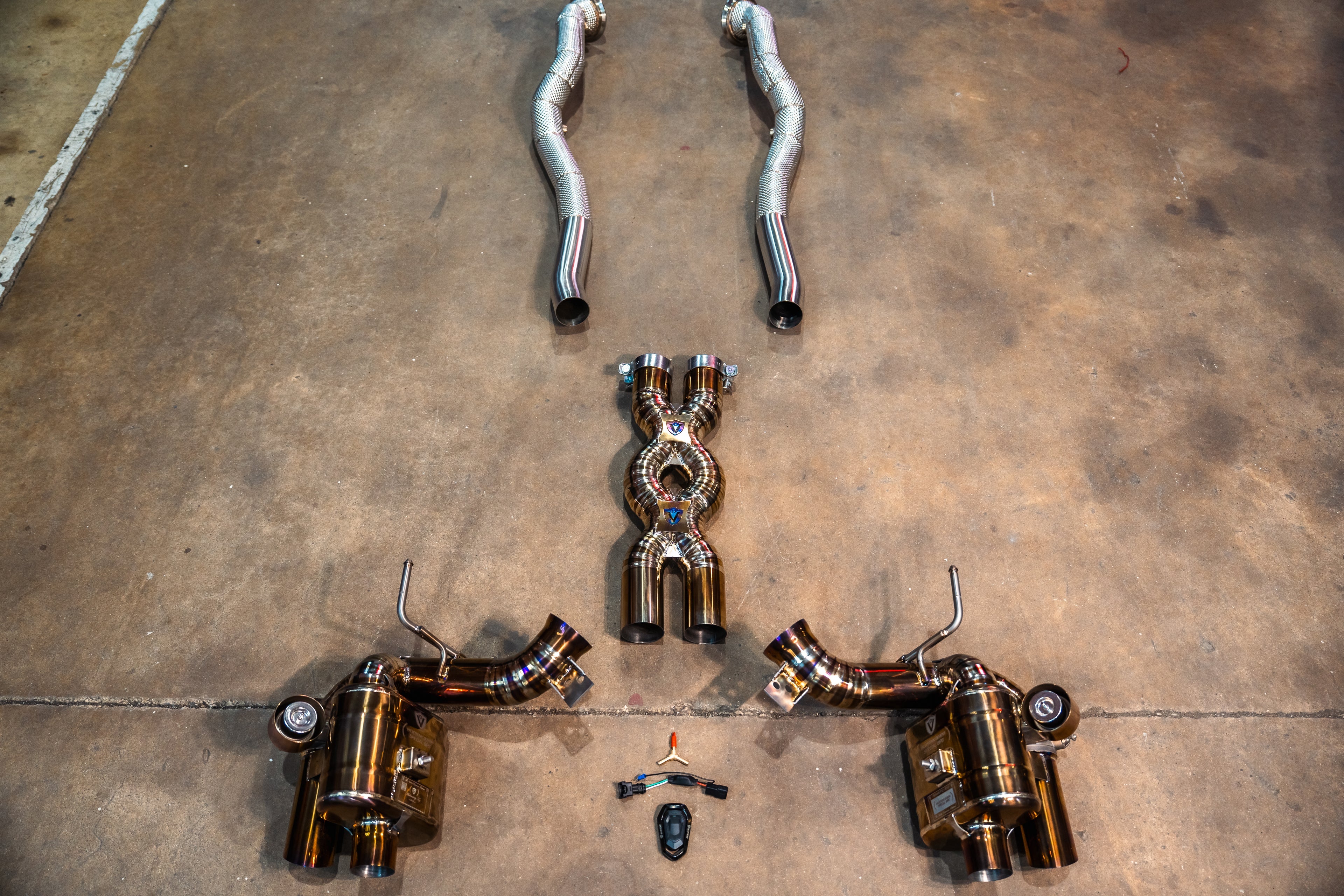 A top-down view of a complete exhaust system featuring a gold muffler, silver mid-pipes with heat shielding, and long-tube headers.