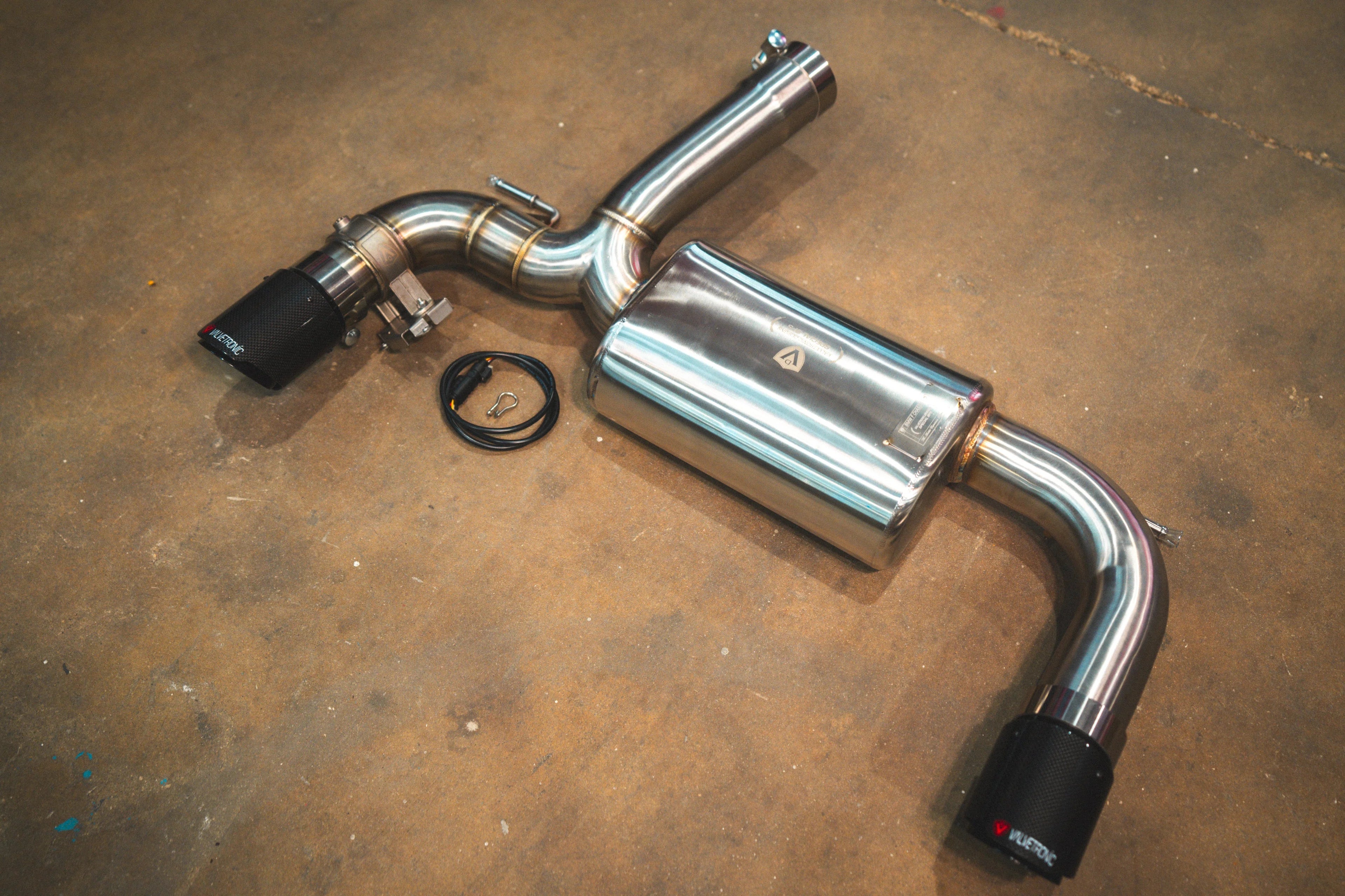 A full overhead view of the valved axle-back exhaust system featuring a central muffler, mandrel-bent piping, and two carbon fiber exhaust tips.