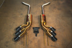 Full layout of the gold-finish exhaust system including long connecting pipes, triple-tip mufflers, and the electronic control module.