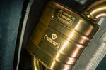 Extreme close-up of a gold exhaust muffler featuring an engraved Valvetronic Designs "Special Ops" plaque and a W204 C63 identification tag.