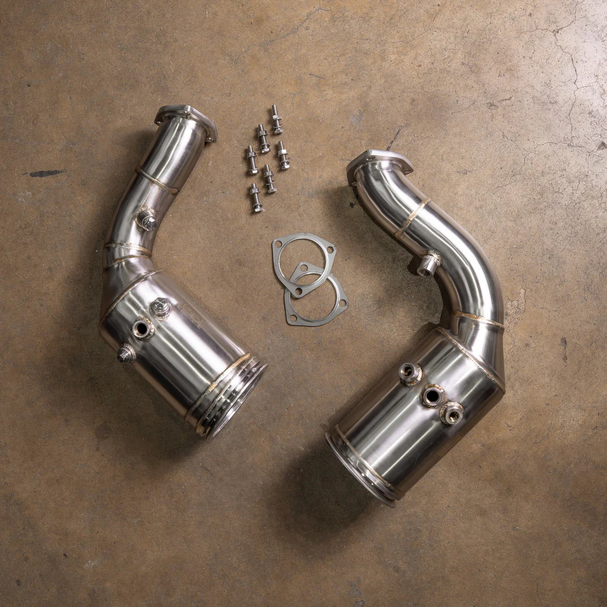 A pair of Valvetronic Designs 400 Cell Catted Downpipes for a 2019-2022 Lamborghini Urus, displayed on a concrete floor with accompanying mounting hardware and gaskets.