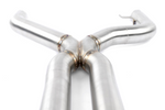 A close-up view of the central X-pipe junction of a stainless steel exhaust system, showing the industrial welded seams where four curved pipes are joined together.