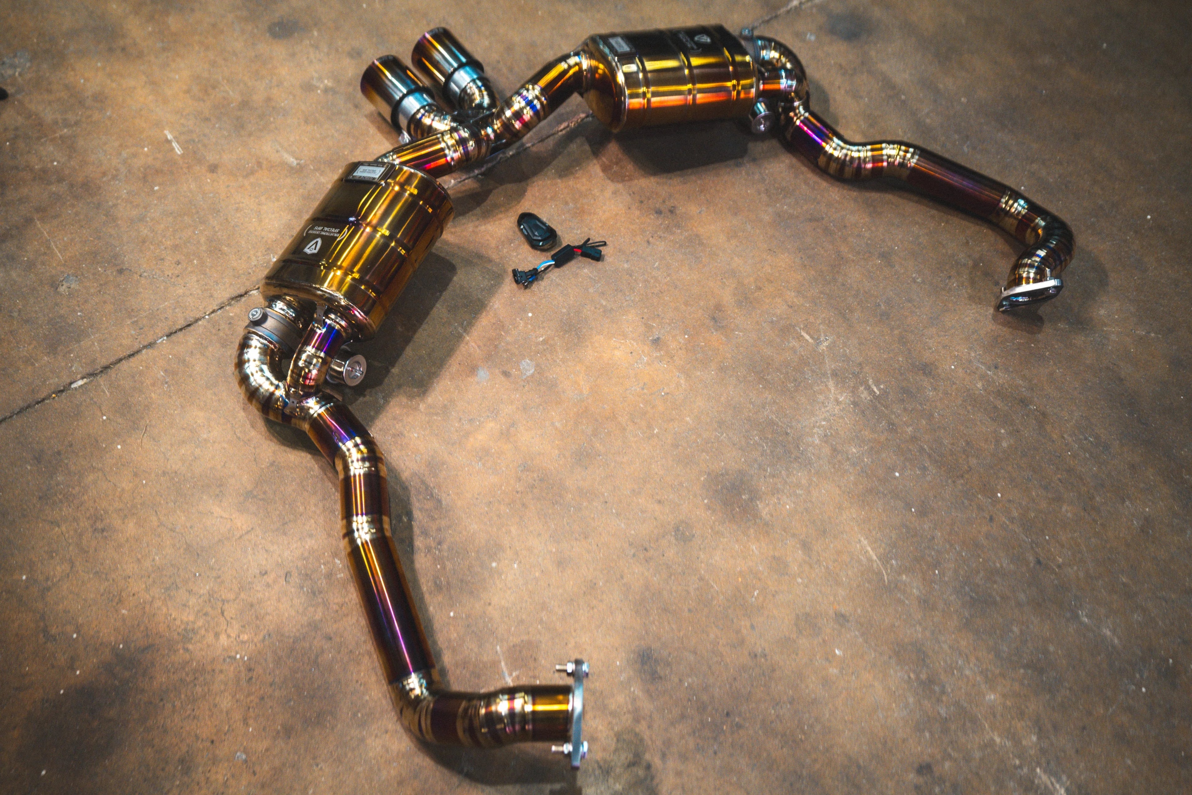 High-angle shot of the complete valved exhaust system displayed on a concrete floor, including the electronic valve controller and wiring harness.