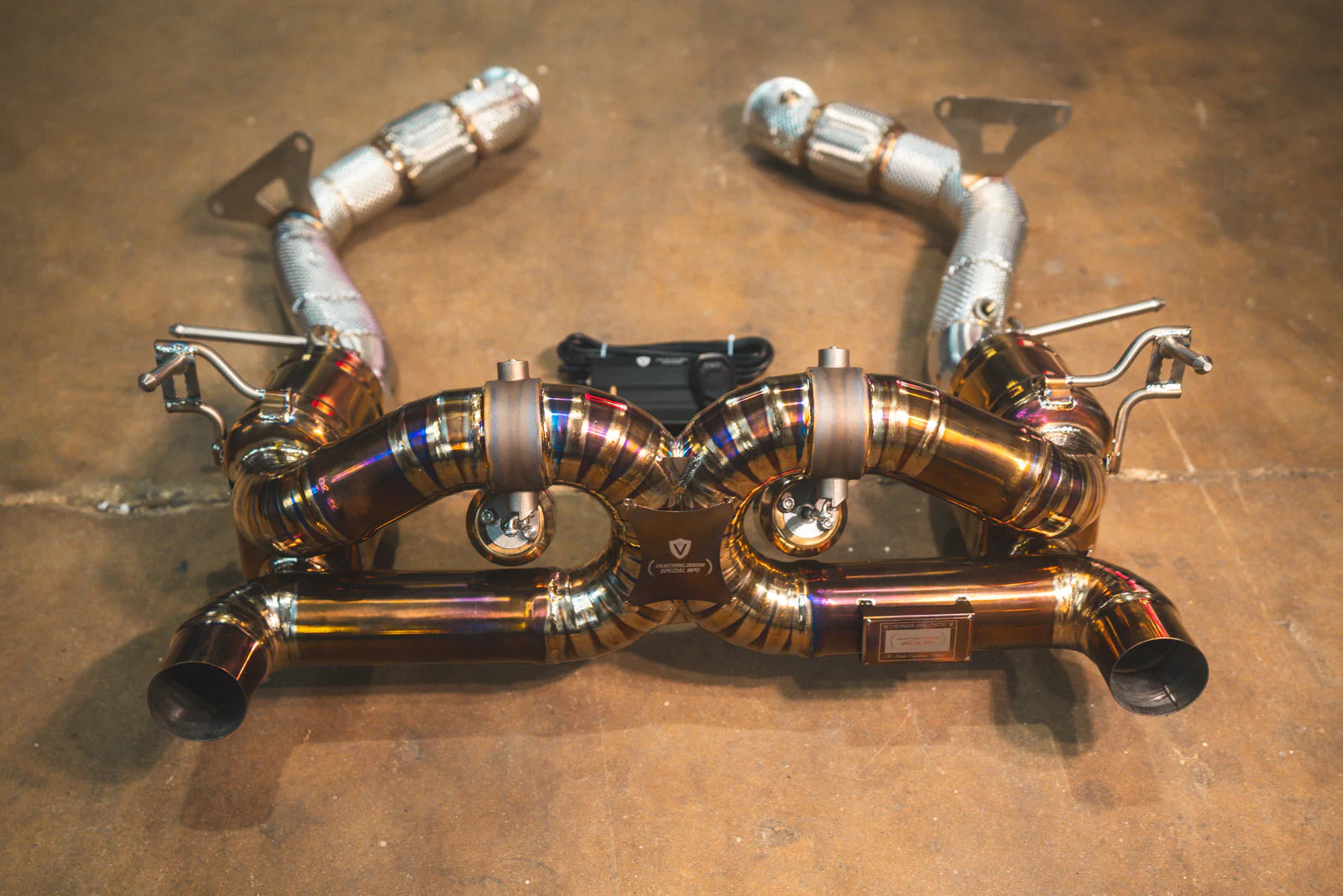 A top-down view of the gold-finish valved exhaust system paired with two silver heat-shielded race pipes and a remote control module.