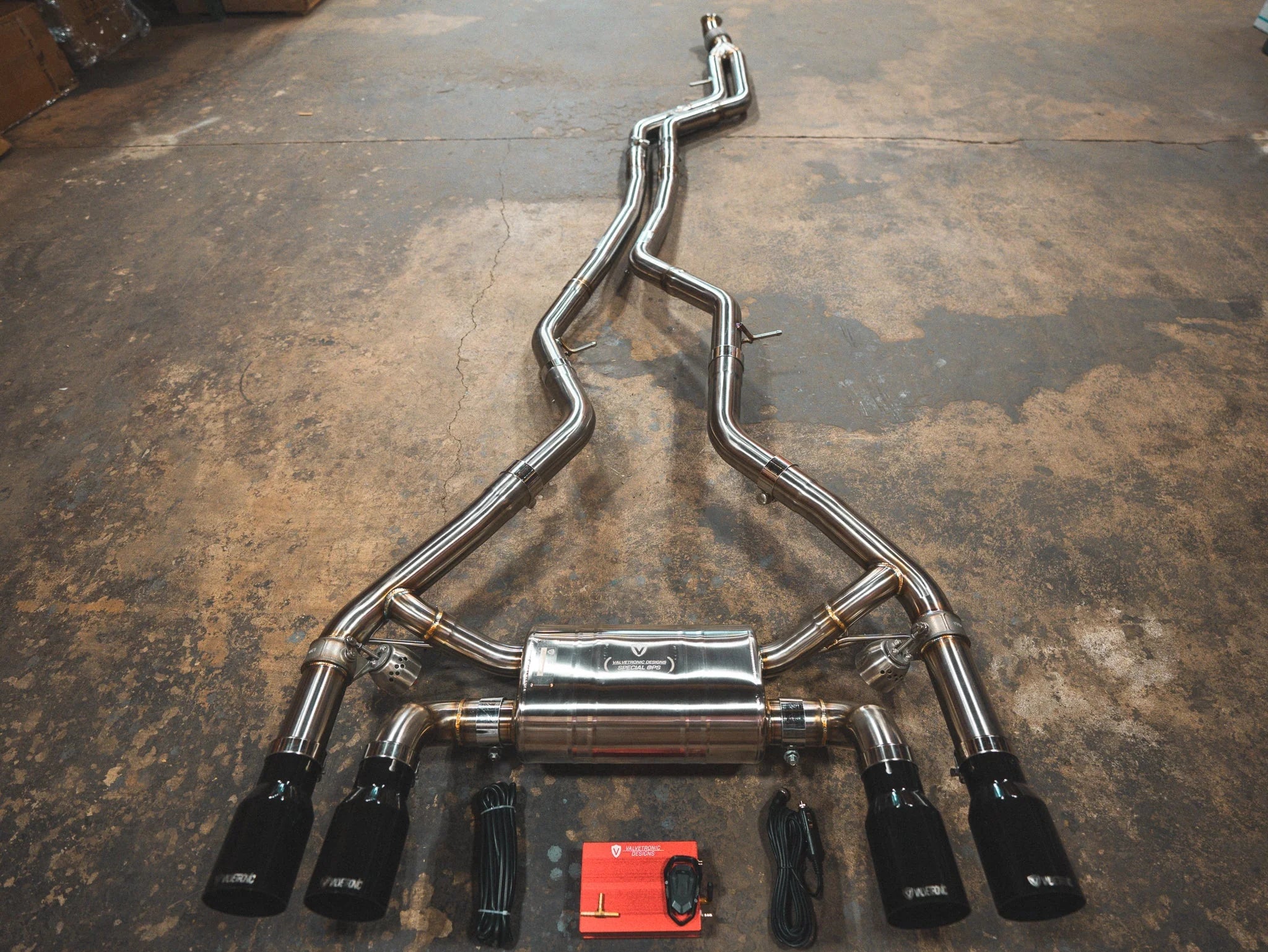 A complete stainless steel valved exhaust system for a BMW M2 featuring a quad-exit configuration with four glossy black exhaust tips and accompanying electronic control hardware.