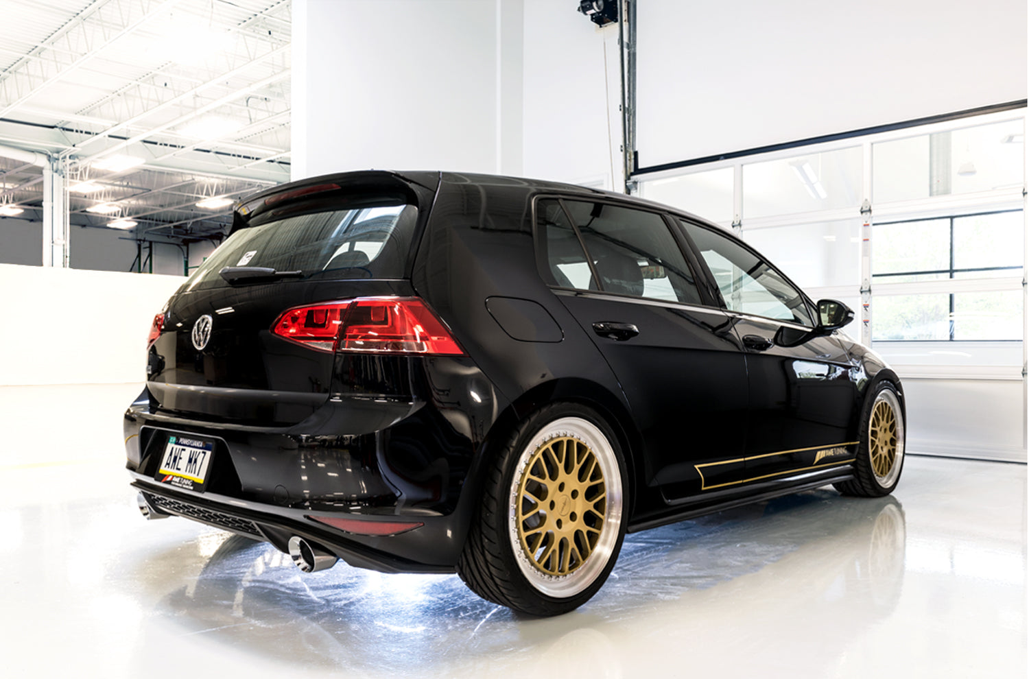 Black Mk7 GTI with gold wheels, rear three-quarter studio view with AWE exhaust tips