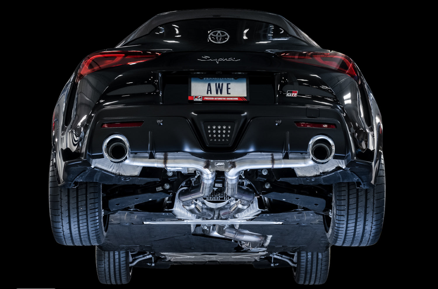 Black A90 GR Supra rear on a black backdrop showing the AWE Track system under the car
