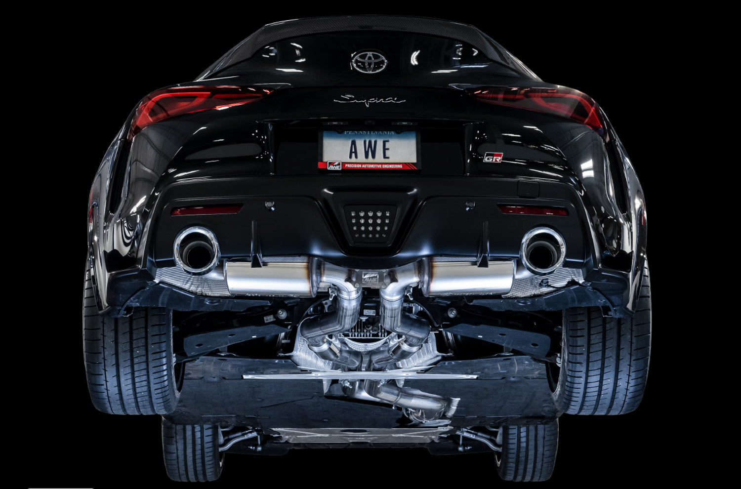 Black A90 Supra rear against a black backdrop with the AWE Touring mufflers visible below