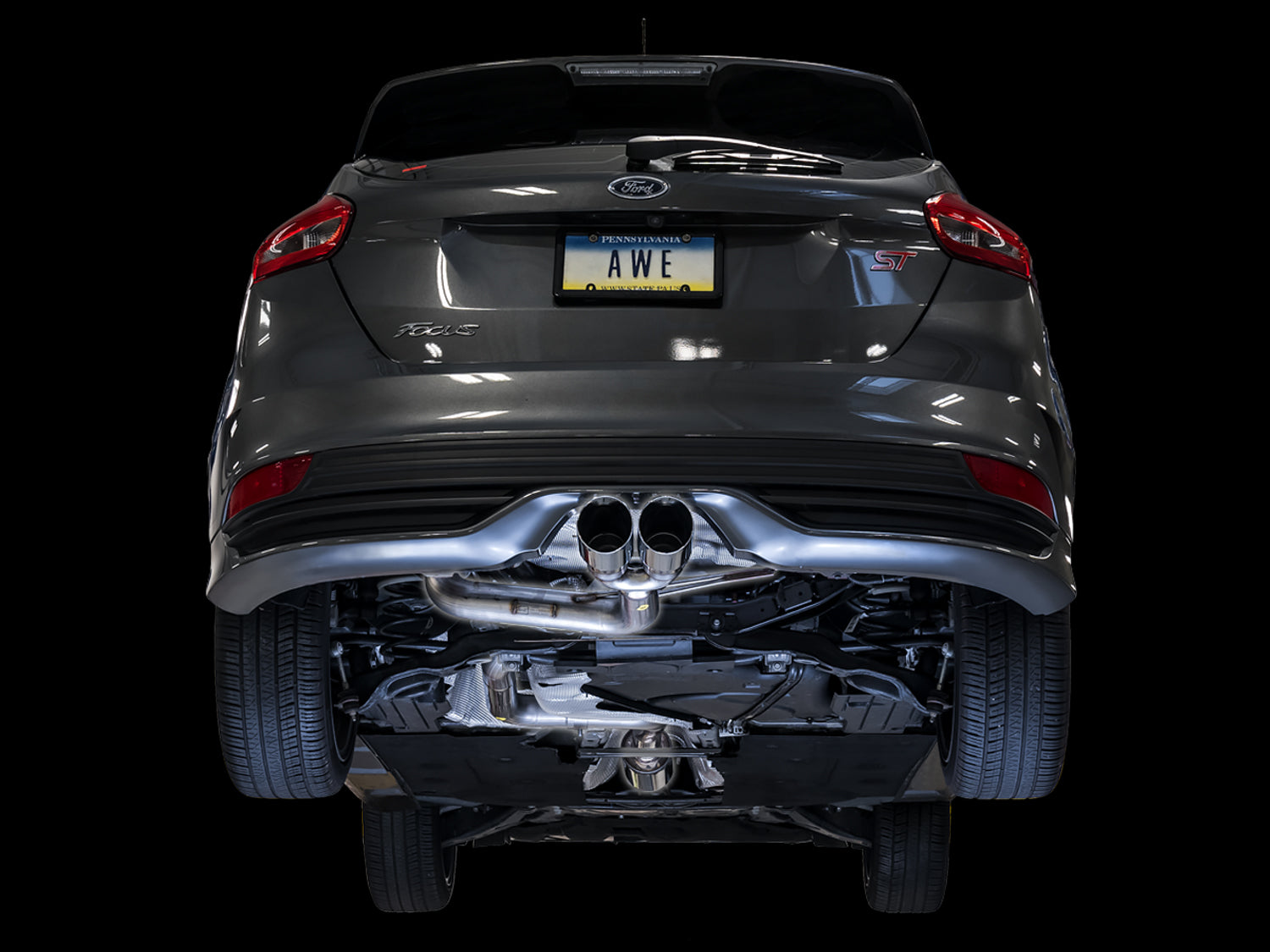 Low rear view of a gray Focus ST on black showing the AWE cat-back routed under the car