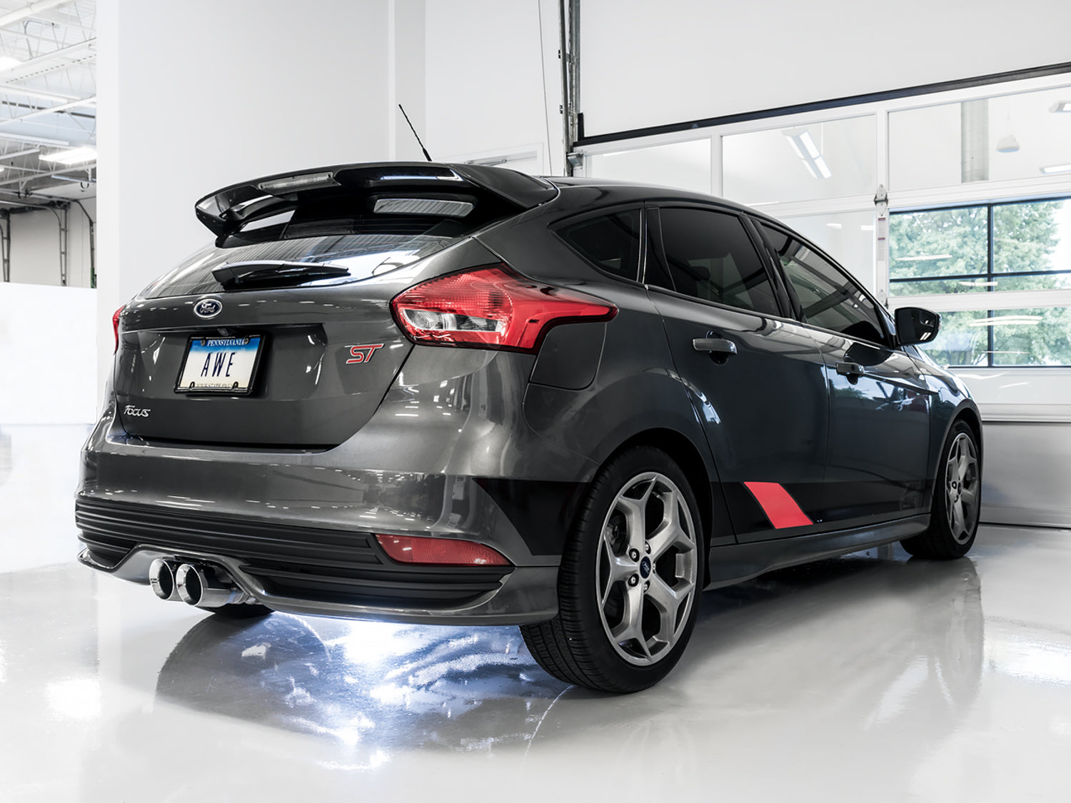 Rear three-quarter view of a gray Focus ST hatchback in a white garage fitted with AWE exhaust