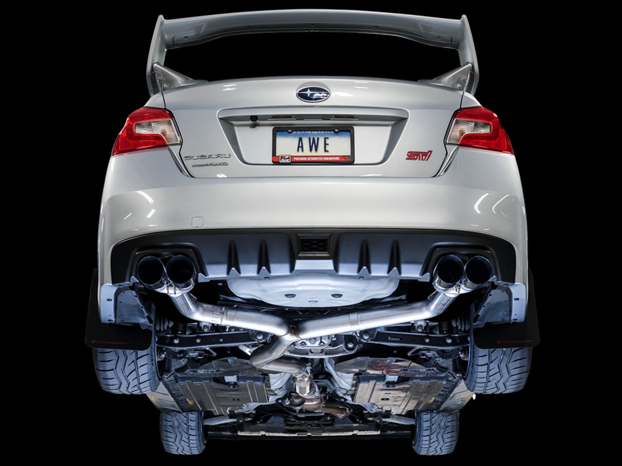 Underside of a white VA WRX STI on a black backdrop showing AWE Track Edition pipework