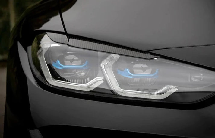 A front close up view of AUTOTECKNIC CARBON FIBER HEADLIGHT COVERS - BMW G80 M3 | G82/ G83 M4 2021+ fitted on a black car