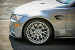 A close up view of a grey BMW and its front wheel fitted with AP Racing by Essex Radi-CAL ENP Competition Brake Kit (Front 9660/372mm)- BMW E90/E92/E93 M3 & 1M Coupe