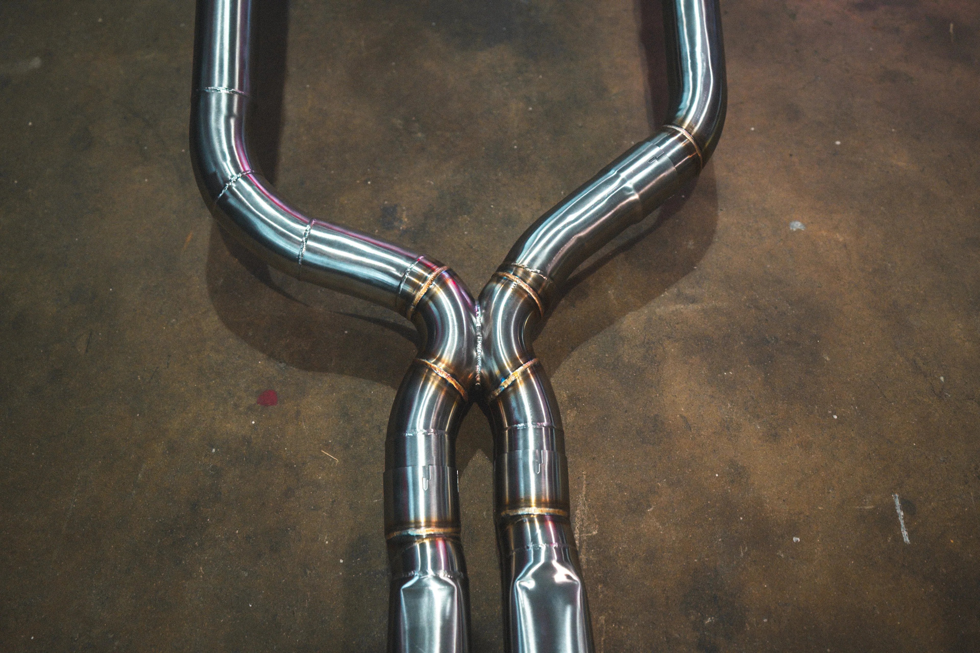 A close-up view of the X-pipe crossover section of the exhaust system, highlighting the precision welds and the transition where the two main pipes merge and then separate.