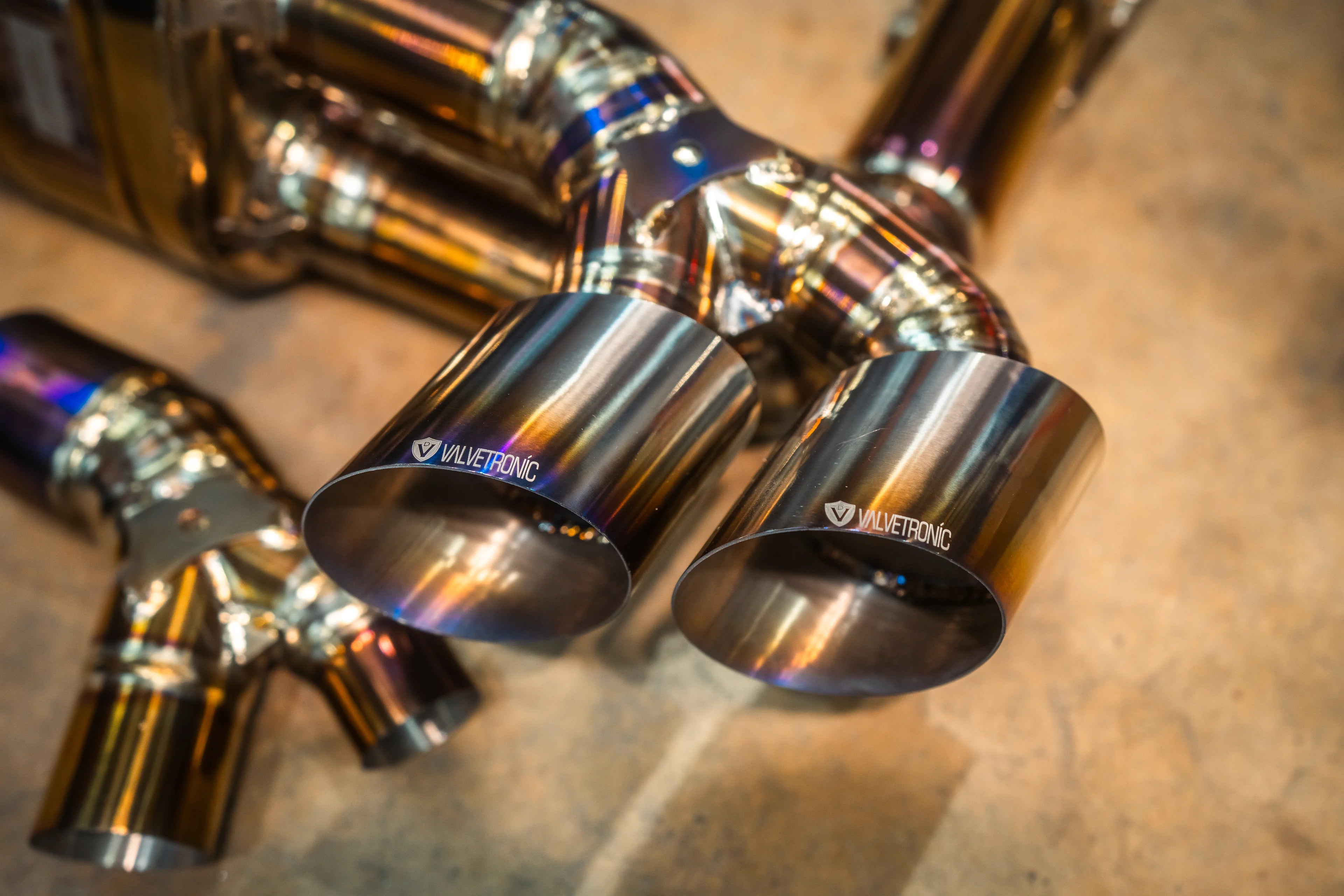 Macro view of dual circular exhaust tips with the "Valvetronic" logo etched on the brushed metal surface.