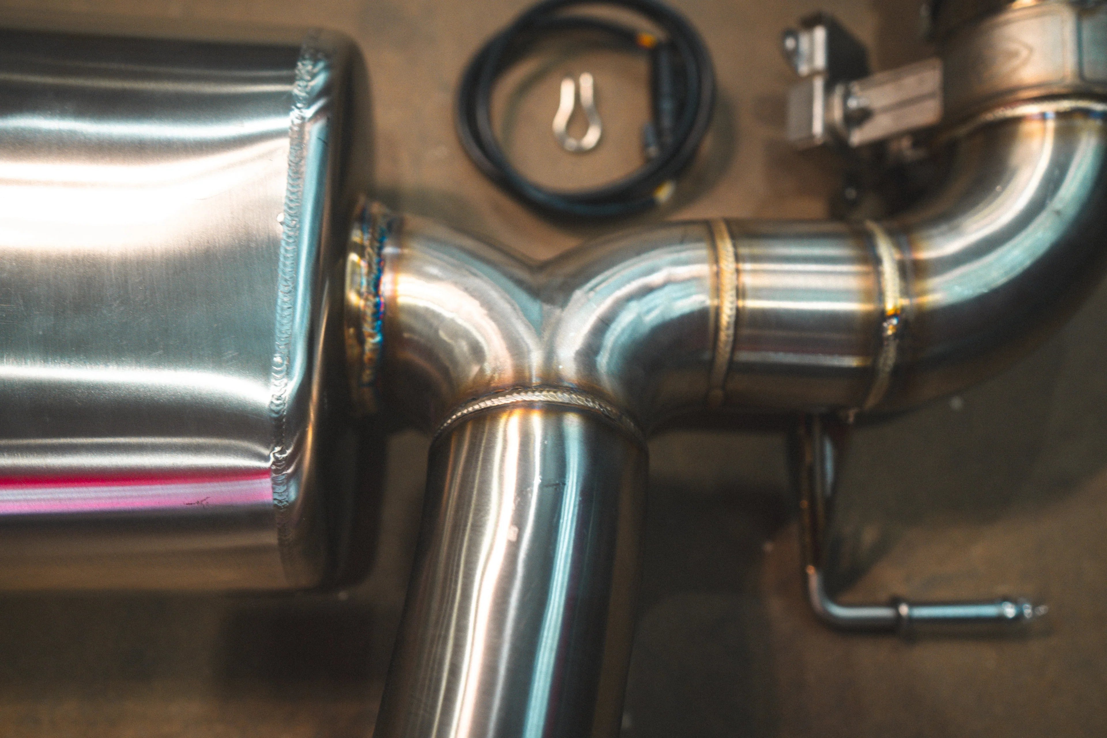 A close-up of the exhaust system's TIG welding points where the stainless steel piping branches into a Y-pipe configuration.