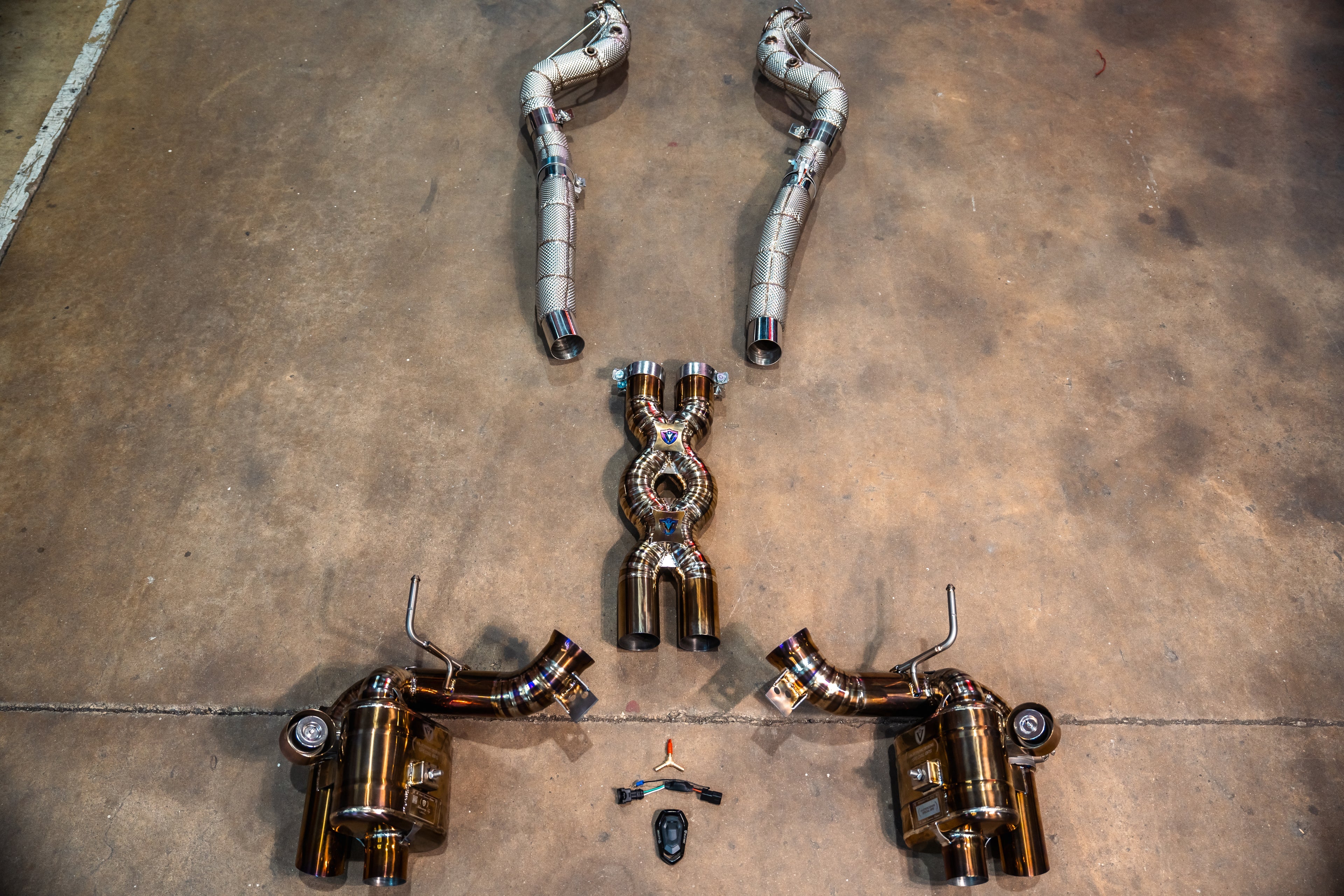 A top-down view of the gold valved muffler connected to two silver mid-pipes with textured heat shielding.