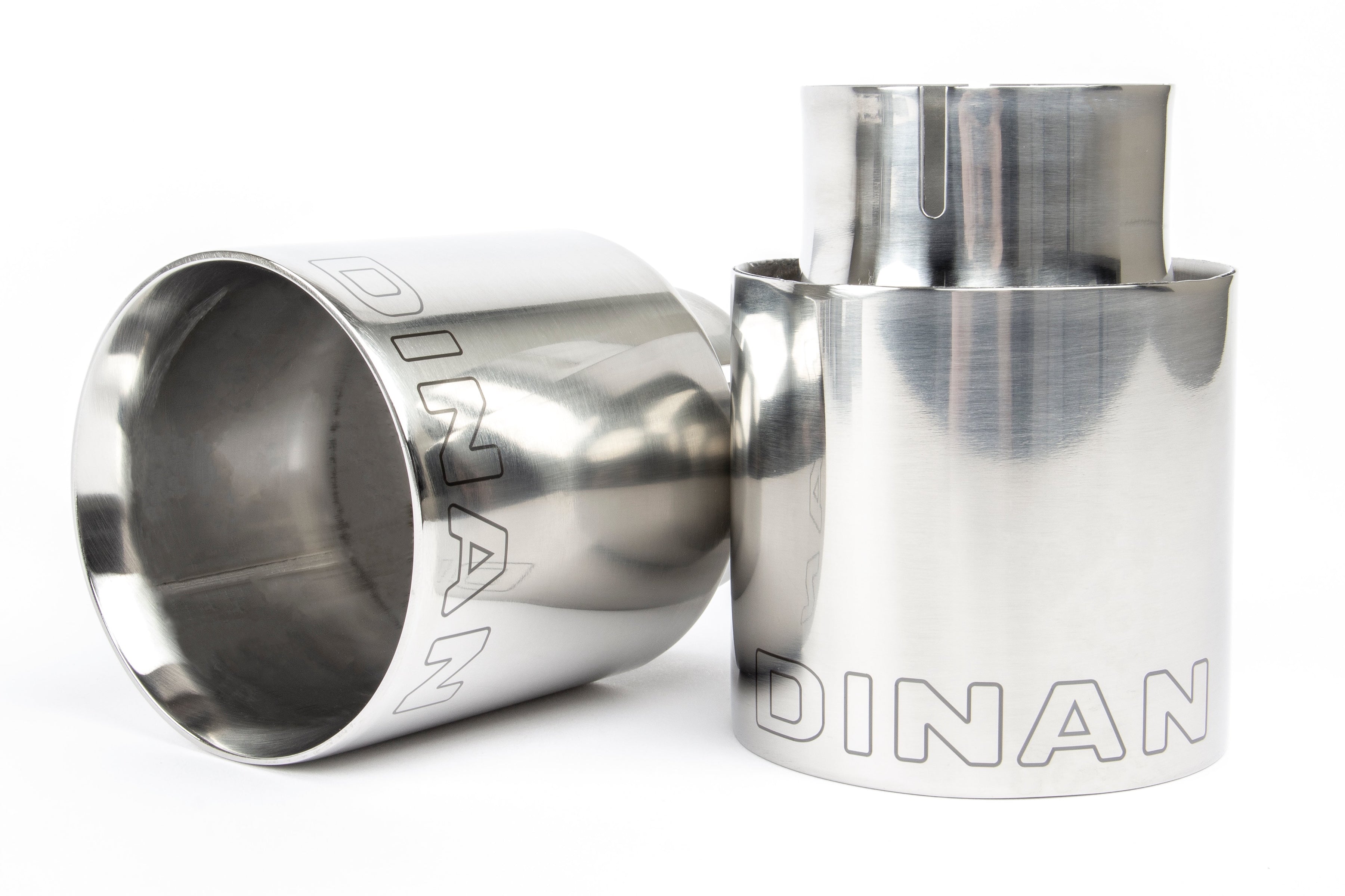 A close-up view of the two polished stainless steel exhaust tips. The image highlights the double-walled, slant-cut design with a mirror finish and the laser-etched Dinan logo on the top of each tip.