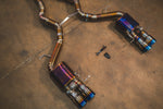 A close-up view of the rear section of the exhaust, featuring two valved mufflers and quad burnt-blue titanium tips.