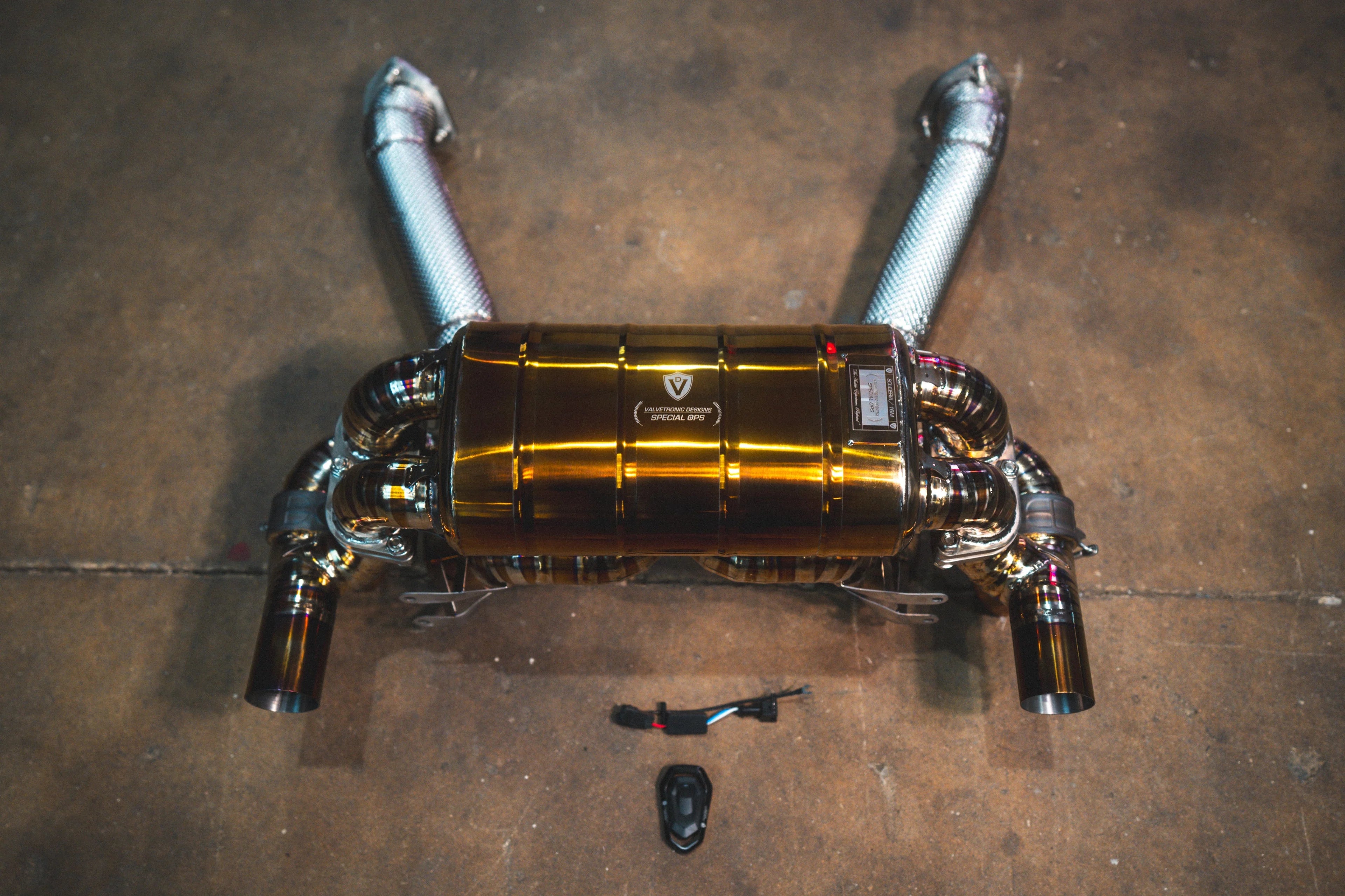 A top-down view of the gold valved muffler connected to two silver mid-pipes featuring textured heat shielding.