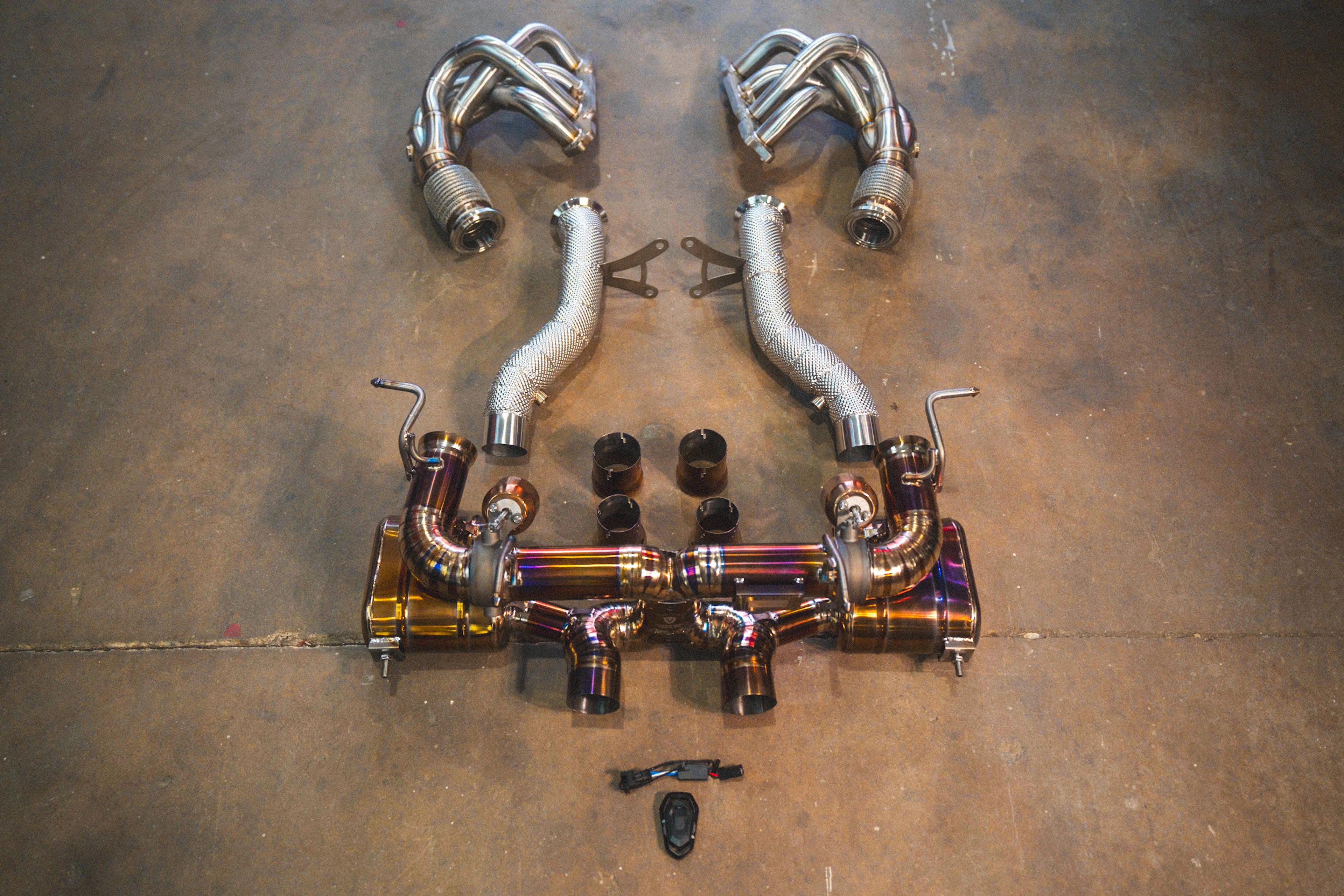 A top-down view of the complete exhaust assembly including gold-finish valved mufflers, silver heat-shielded front pipes, and long-tube headers.