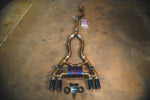 A full titanium valved exhaust system laid out on a concrete floor, featuring four gloss black exhaust tips and a central purple/blue heat-treated muffler.