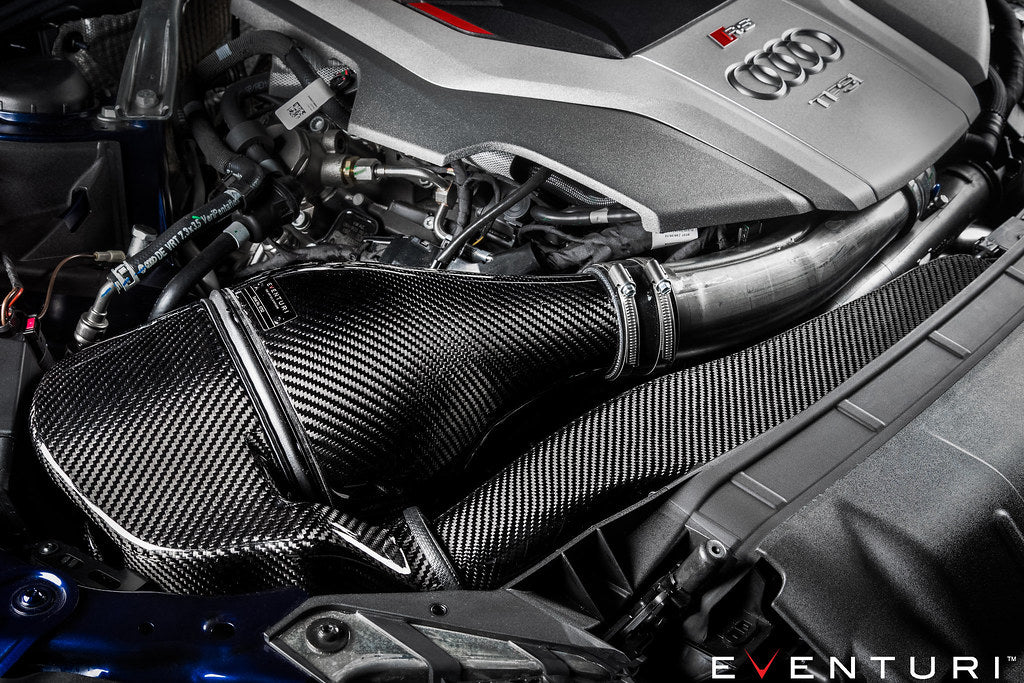 Carbon fiber intake system with cylindrical air filter installed in engine bay showing textured weave pattern and aluminum tubing - Eventuri intake for Audi B9 RS5