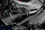 Carbon fiber intake system with cylindrical air filter installed in engine bay showing textured weave pattern and aluminum tubing - Eventuri intake for Audi B9 RS5