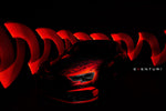 Black carbon fiber headlamp race duct installed on vehicle front bumper with dramatic red lighting effects - Eventuri headlamp race duct for Audi RS3
